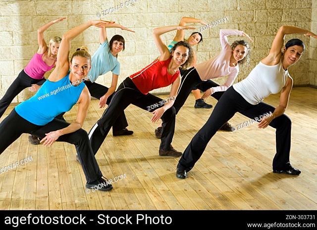 A group of women working out in the fitness club making stretching exercise. They're smiling and looking at camera. Front view