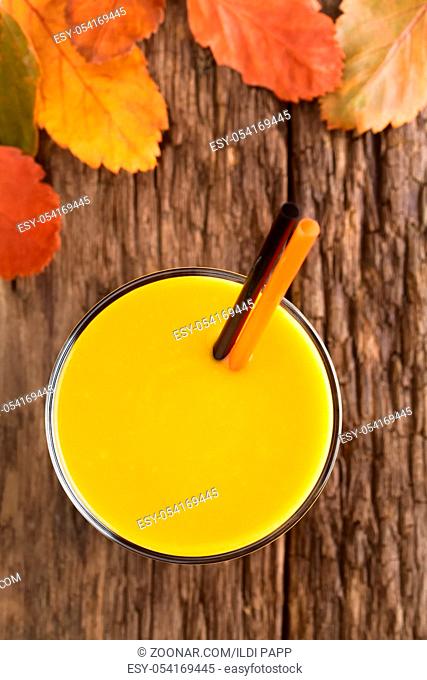 Fresh homemade pumpkin smoothie in glass with drinking straws, photographed overhead on wood with colorful autumn leaves