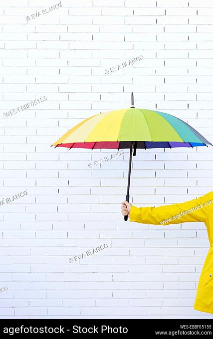 Woman holding multi colored umbrella in front of brick wall