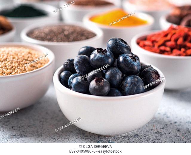 Blueberries in small white bowl and other superfoods on background. Selective focus. Different superfoods ingredients. Concept and illustration for superfood...