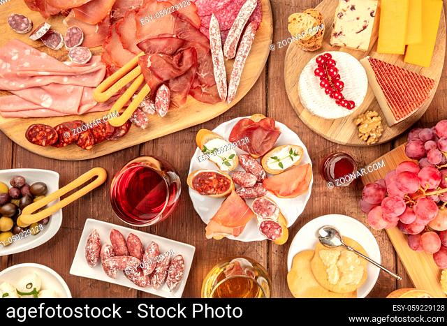 Charcuterie Tasting. A photo of many different sausages and hams, deli meats, and a cheese platter, shot from above on a rustic background with a glass of red...