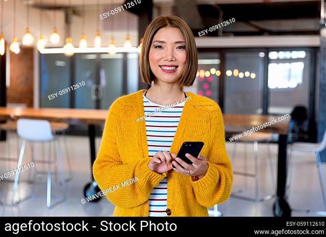 Portrait of asian smiling businesswoman standing holding and using a smartphone