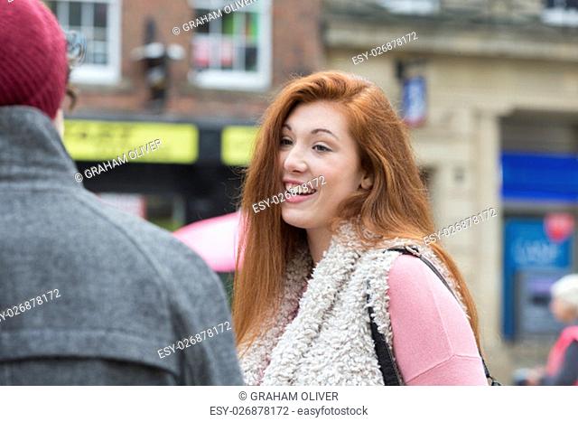 A happy female student smiles as she stands amongst her friends outdoors. They are taking a break from university in the city centre