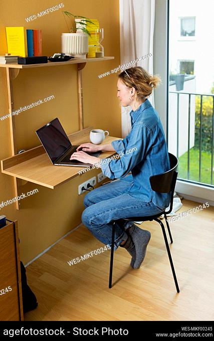 Freelancer wearing denim shirt working on laptop at home office