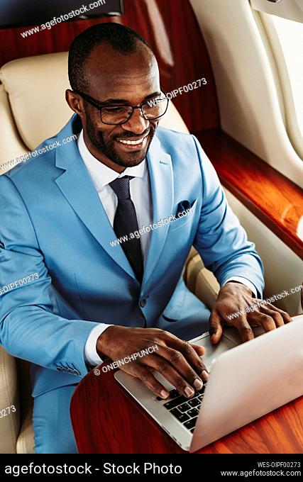 Smiling male entrepreneur working on laptop in private jet