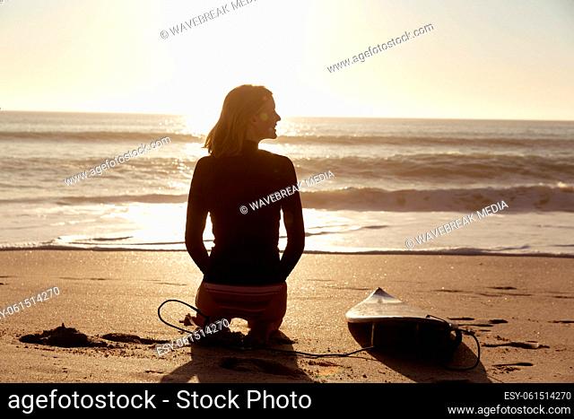 Woman with surfboard sitting on the beach