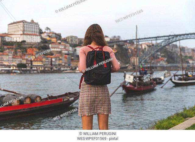 Back view of young woman with backpack standing in front of Douro River, Porto, Portugal