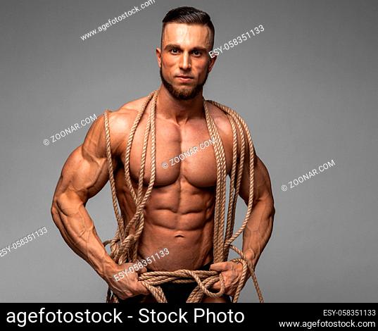 Strong Muscular Men Trapped in Ropes Trying to break lose. Bodybuilder Trapped in Ropes on gray background. Studio shoot