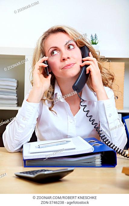 Gestresste Frau im Büro telefoniert mit zwei Telefonen gleichzeitig