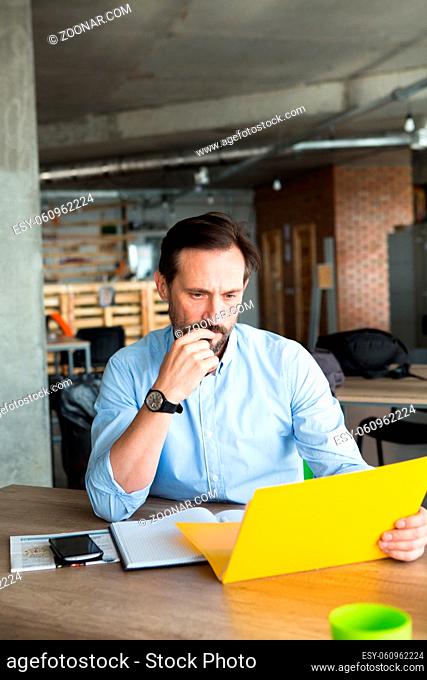 Confident businessman looking through documents of foreign partners in office interior. Executive man thinking about agreement or contract