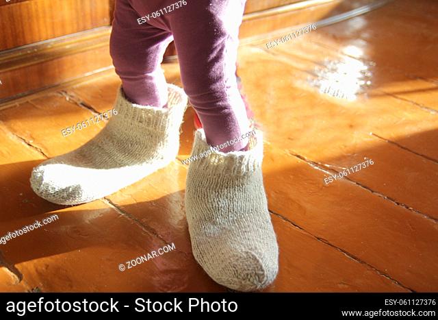 Little girl trying on dad's wool socks at home, close up