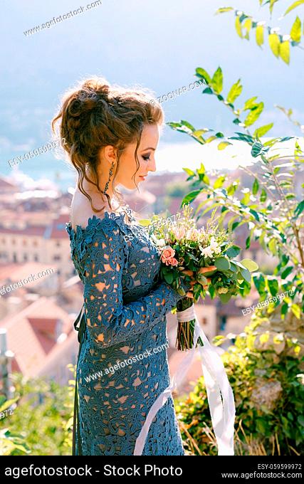 A bride in a blue dress stands with a bouquet in her hands, behind her opens a view of the old town of Kotor . High quality photo
