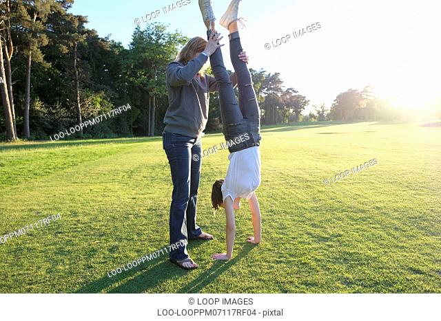 A woman helping her daughter with a handstand on a sunlit day