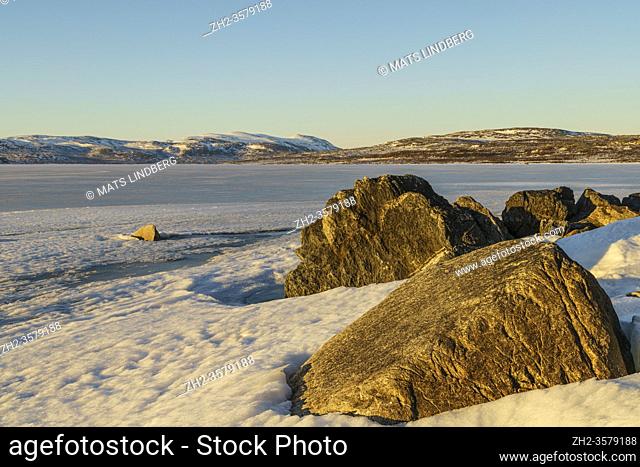 Snowy landscape in spring time with mountains in background, frozen lake Torneträsk, big rocks in foreground, Kiruna county, Swedish Lapland, Sweden