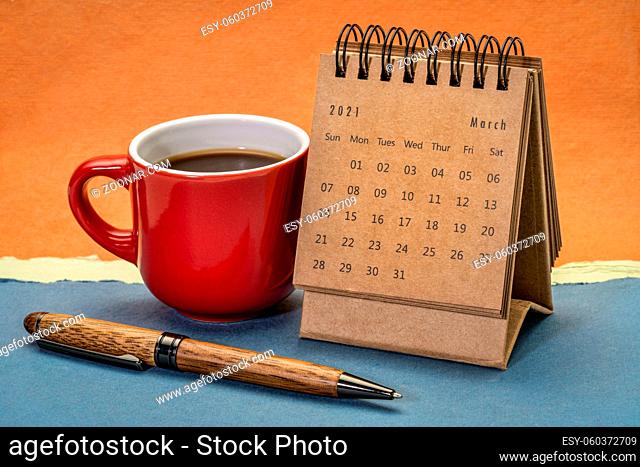 March 2021 - spiral desktop calendar against abstract paper landscape with a cup of coffee and pen, time and business concept
