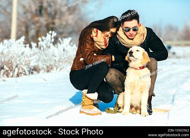 Cute young hipster couple having fun in winter park with their dog on a bright day and smiling