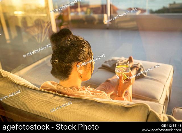 Woman relaxing with water on sunny patio sofa