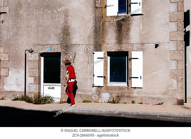 Woman walking on street passing by stone house doorway. Morlaix, Brittany, France