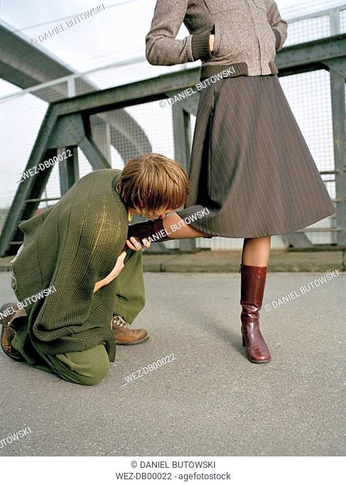 Kneeling man kissing foot of woman