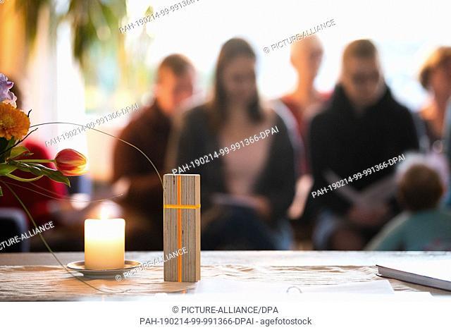14 February 2019, Bavaria, Bayreuth: A sculpture with a cross stands on a living room table next to a candle. Around 20 adults and children have gathered at the...