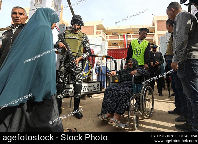 10 December 2023, Egypt, Sheikh Zuweid: A policeman helps an elderly woman in a wheelchair at a polling station during the presidential election