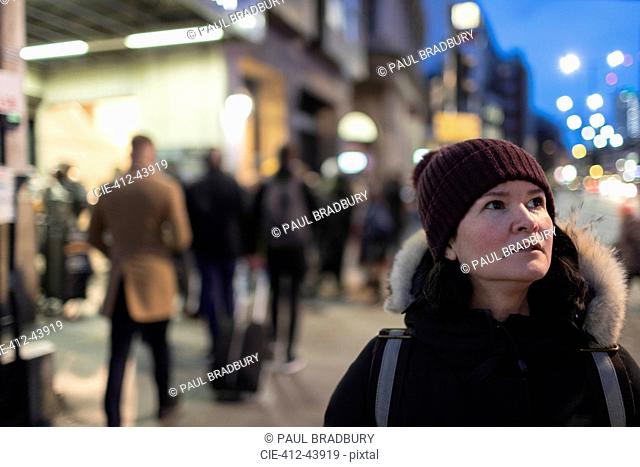 Woman in warm clothing standing on urban sidewalk at night