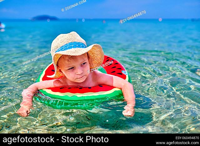 Two year old toddler boy on beach swimming with inflatable ring