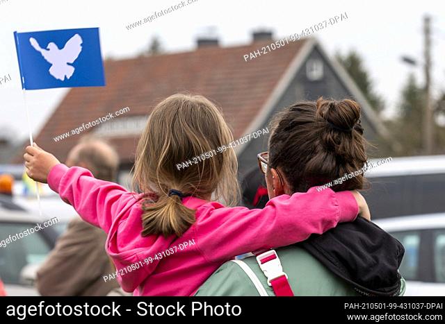 01 May 2021, Saxony, Großschönau: After the end of a motorcade, a little girl waves a blue flag with a dove of peace at the final rally