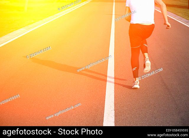Jogging man along road. Closeup of male in running shoes going for run on road at sunrise or sunset. Fitness or sport concept. Toned