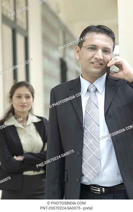 Portrait of a businessman talking on a mobile phone with a businesswoman standing behind him
