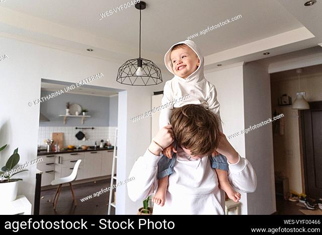 Boy carrying younger sibling on shoulder at home