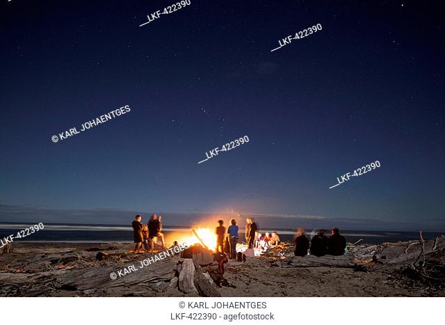 Bonfire with driftwood on the beach, group of people around a bonfire, west coast, South Island, New Zealand