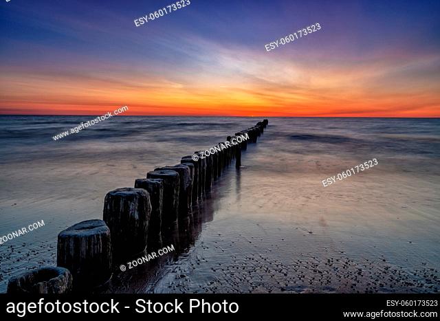 long exposure view of an ocean sunset with sandy beach and wooden pylon storm groin in the foreground