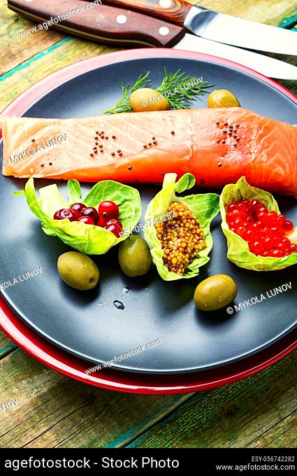 Salted salmon on a plate garnished with red caviar, olive and cranberries
