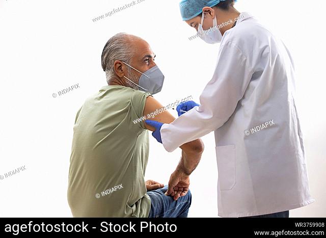 AN OLD MAN WEARING FACE MASK BEING VACCINATED BY A MEDICAL PROFESSIONAL