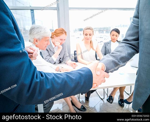 Handshake of business partners after discussion of the financial reports, their team on background