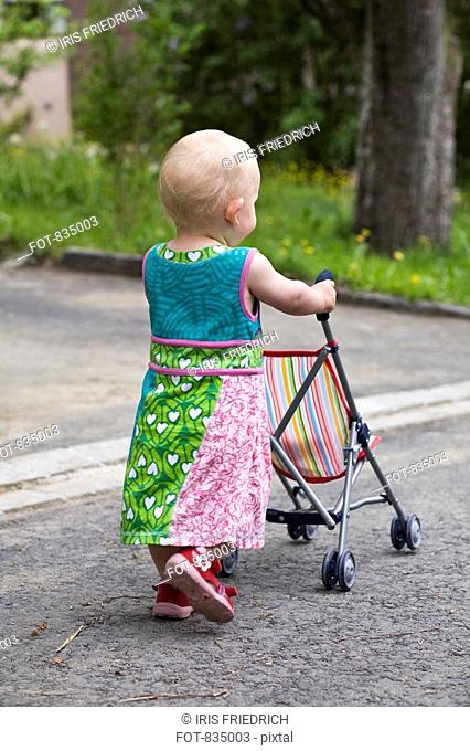 A toddler pushing a baby stroller, rear view
