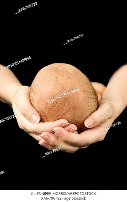 A mother's hands cradle a fair-haired newborn baby's head against a black background