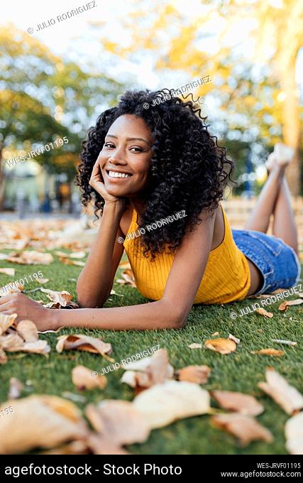 Happy young woman with curly hair lying on grass at park