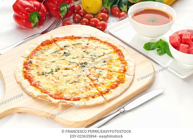 Italian original thin crust pizza Margherita with gazpacho soup and watermelon on side, and vegetables on background