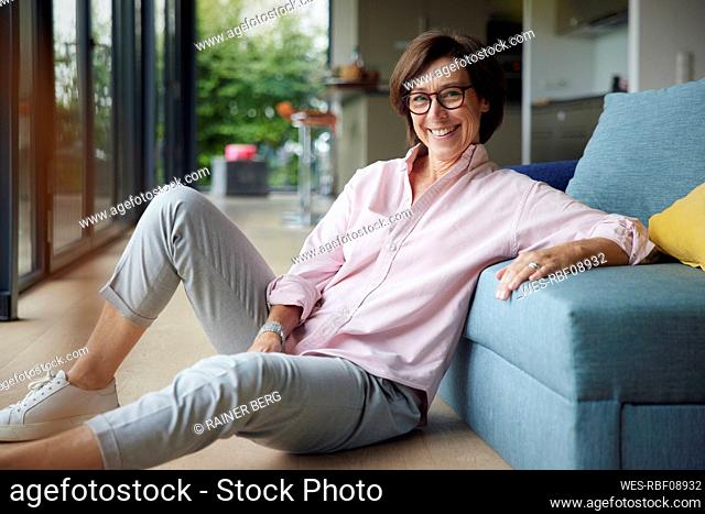 Happy woman sitting on floor by sofa at home