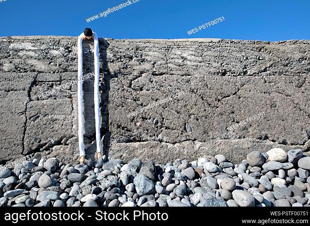 Woman with artificial long hands bending over retaining wall at beach