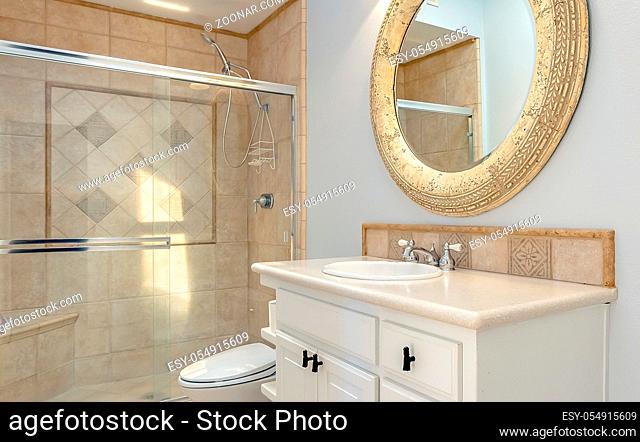 Bathroom with tub shower and glass doors in luxury apartment. Professionally installed brown tile sits with light coming in from a sky light and a round mirror...