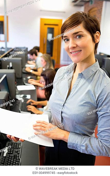 Teacher standing at the computer room holding papers while smiling
