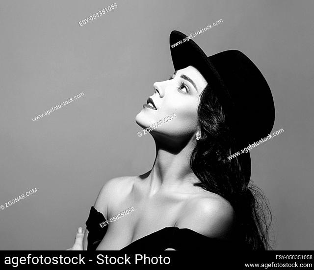 Profile portrait of a beautiful elegant brunette lady woman with long hair wearing a black hat and looks up. Black and white