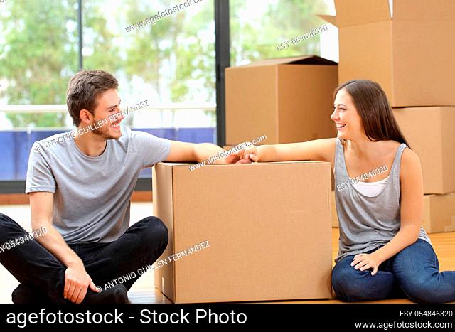 Happy couple looking at each other moving to new home surrounded by boxes sitting on the floor