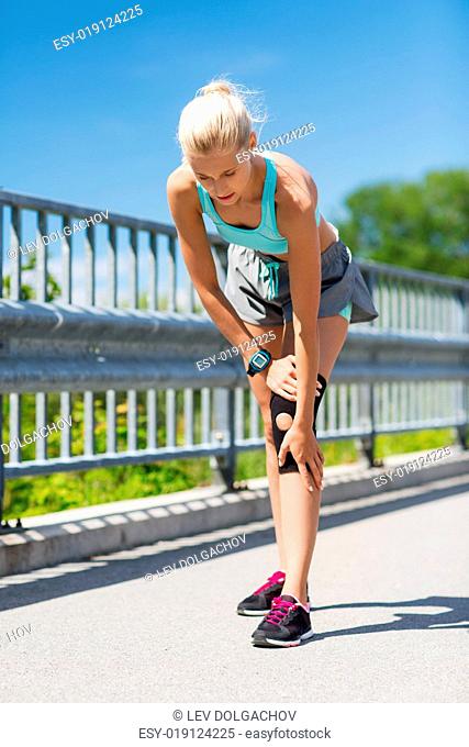 fitness, sport, exercising and healthy lifestyle concept - young woman with injured knee or leg outdoors