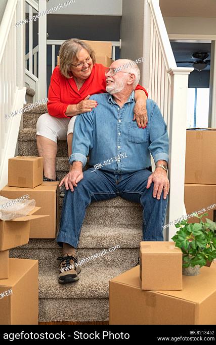 Senior couple resting on stairs surrounded by moving boxes