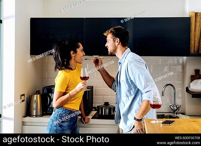 Happy young couple cooking and drinking wine in the kitchen at home together