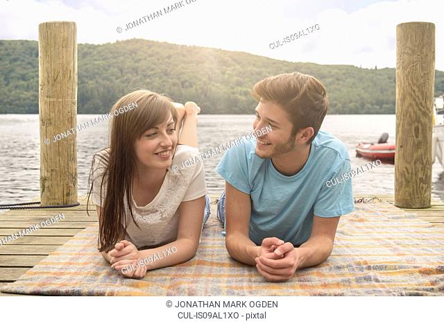 Young smiling couple lying on blanket on lakeside jetty